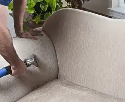 Professional upholstery cleaner deep-cleaning a fabric sofa with a handheld extraction tool and hose in Clearwater, FL.